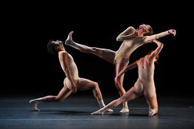 three dancers in nude leotards, one is kicking in the air