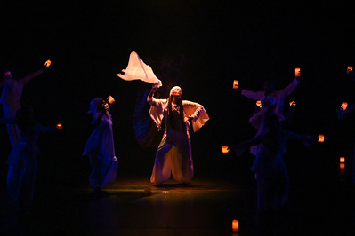 A dancer waving with fabric on stage surrounded by candles 