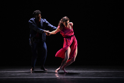 two dancers pulling each other, one male African American dancer wearing a blue jacket and one caucasian female dancers wearing a pink dress