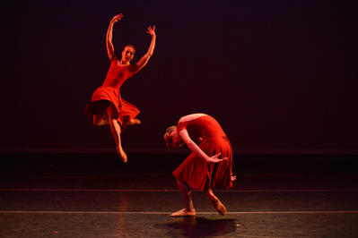 two female dancers in red dresses, one hunching and one jumping