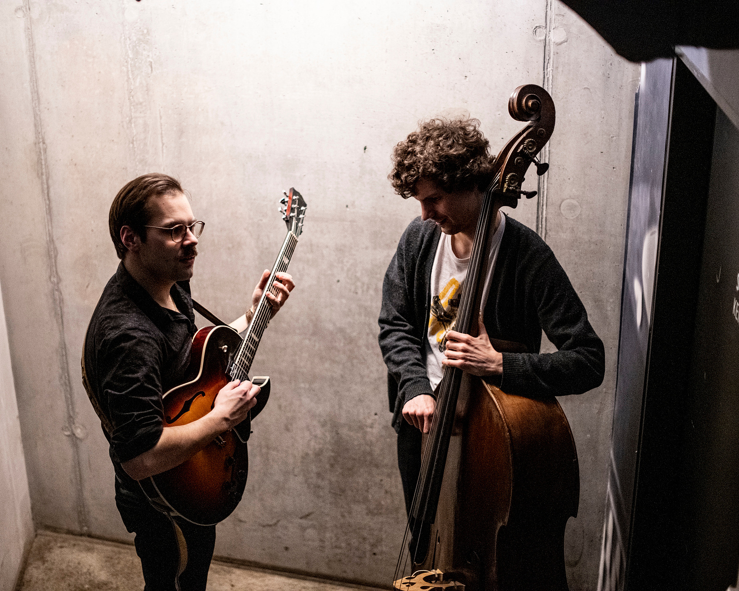 two musicians waiting in backstage in front of a stone wall