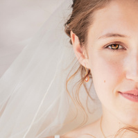 This portrait captures a poetic stillness—half of a young bride's face softly lit, framed by delicate wisps of hair and the gentle fall of her veil. There's a quiet strength and vulnerability in her expression, evoking the romantic resilience of Les Mis
