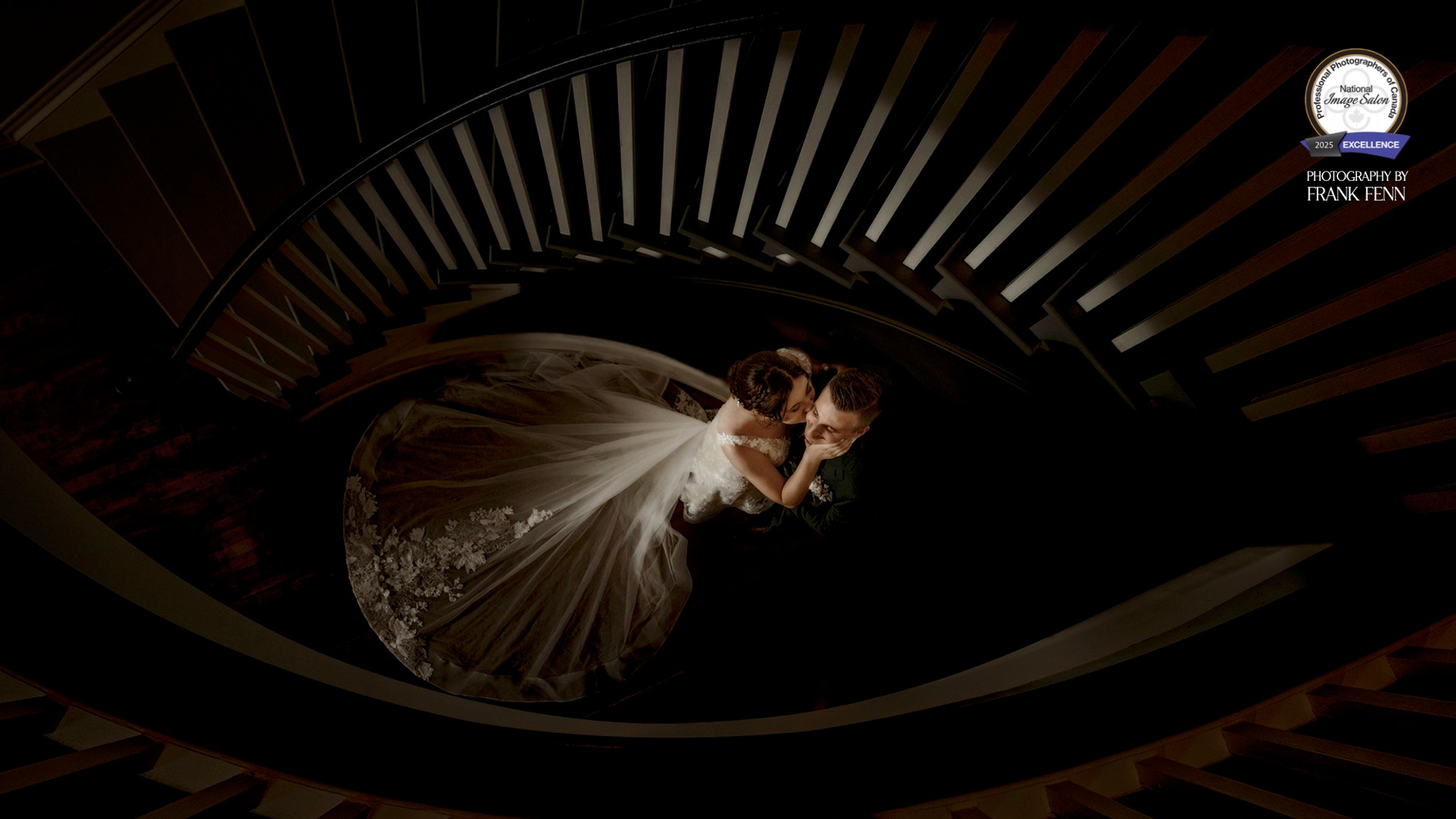 This stunning wedding day image showcases a romantic moment between the bride and groom on the grand spiral staircase at The Opinicon in Ontario. Shot from above, the photo highlights the intricate lace detail of the bride’s flowing gown.
