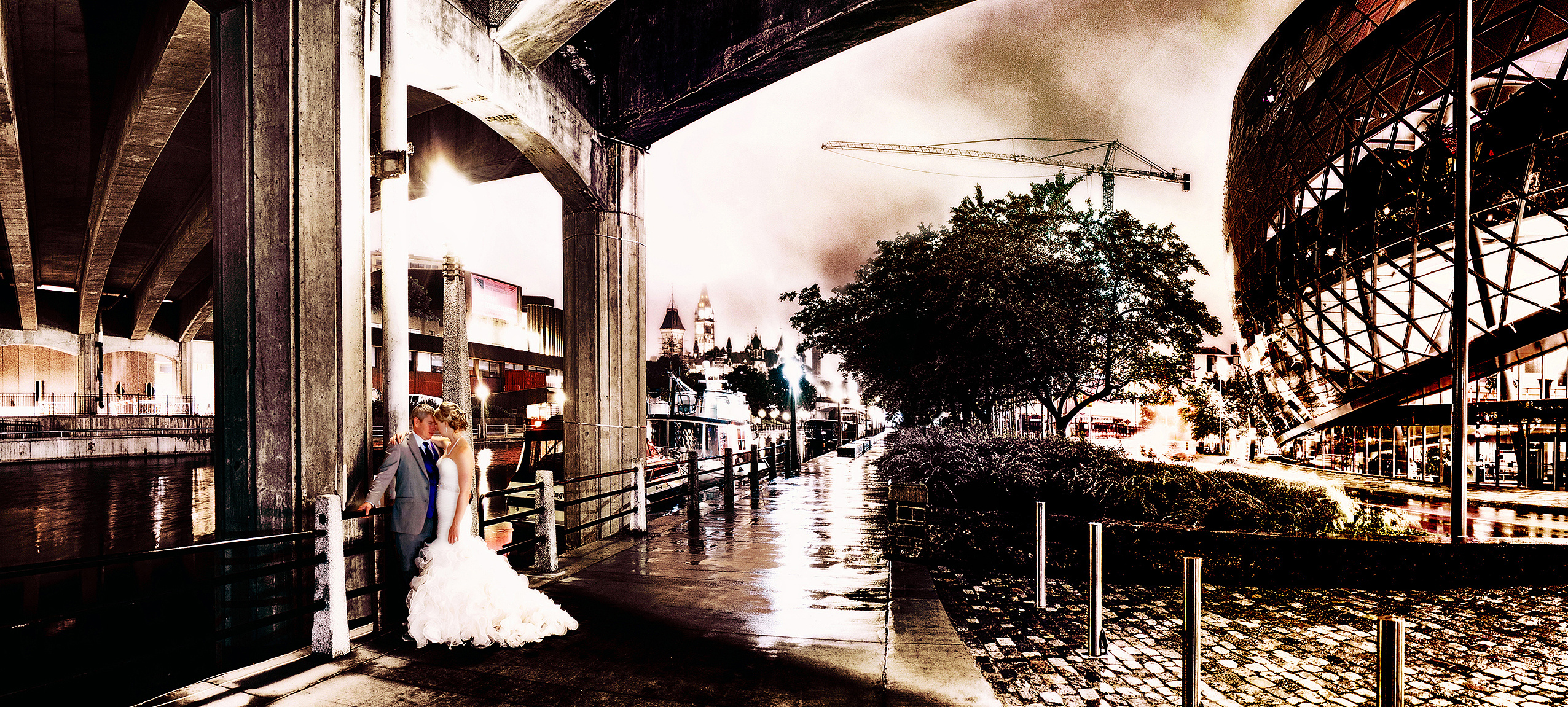 This enchanting nighttime photograph captures a romantic moment as a newlywed couple shares an intimate embrace under the shelter of a historic stone bridge in downtown Ottawa. 
