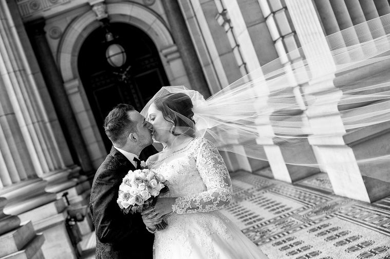 Bride and groom are kissing at Melbourne Parliament House. The groom is wearing a classic floral suit from Politic and the bride is wearing a J'Aton Couture dress.