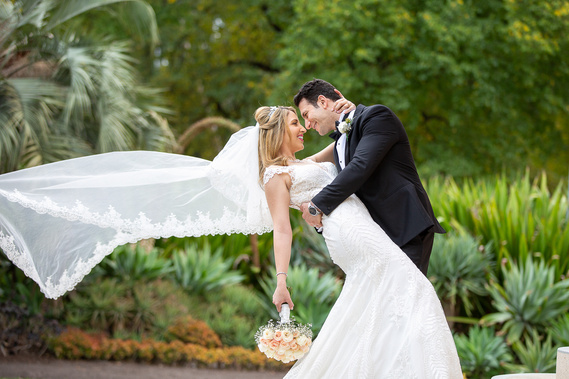 The groom is enjoying a moment of carefreeness with his bride in the Royal Botanical Gardens in Melbourne. The groom is wearing a black suit and is very happy.