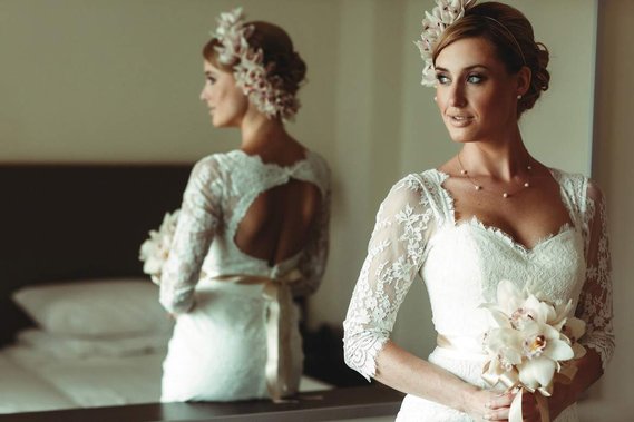 Beautiful bride looking out the window in front of the mirror. Bride is wearing a couture ivory dress with wedding bouquet. 