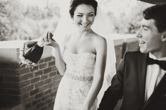 The bride is walking with her groom, holding a bridal bouquet. The person is wearing a J'Aton Couture dress. The other person is wearing a black suit.