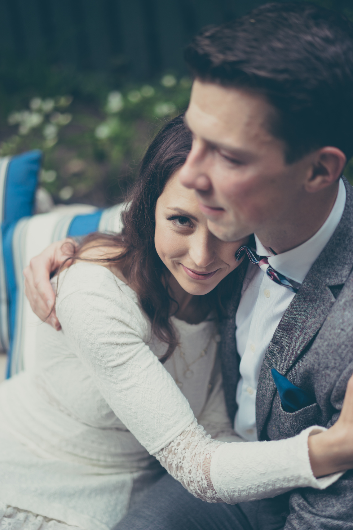 The bride is leaning on a park bench in the Carlton Gardens in Melbourne against her groom. The bride is wearing a J'Aton Couture dress. The groom is wearing a Ferrari suit.