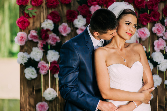 The groom is hugging his bride in front of a tree that is decorated with flowers.