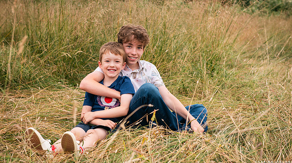 Two brothers sit on the grass together.