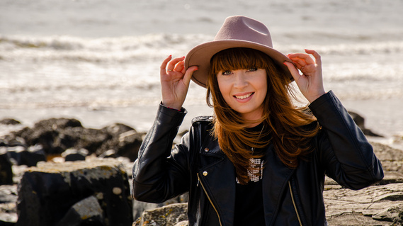 Personal branding photographer Karina Lyburn on a beach holding onto her hat, by Anne Lyburn