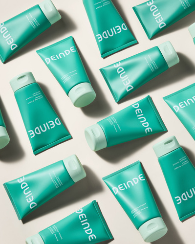 A dynamic flat lay composition featuring an abundance of Deinde skincare tubes, arranged with precision and directional lighting to emphasize product repetition and branding. Photographed by Los Angeles product photographer Alex Kapustin at Rig Studio LA.