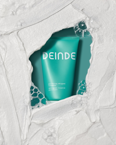 A conceptual product shot featuring Deinde skincare emerging from textured cream, symbolizing deep hydration and skin renewal. Photographed by Los Angeles product photographer Alex Kapustin at Rig Studio LA.