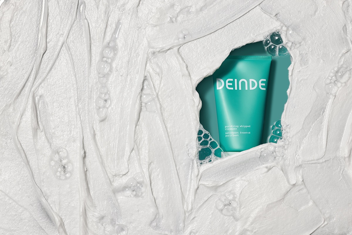 A conceptual product shot featuring Deinde skincare emerging from textured cream, symbolizing deep hydration and skin renewal. Photographed by Los Angeles product photographer Alex Kapustin at Rig Studio LA.