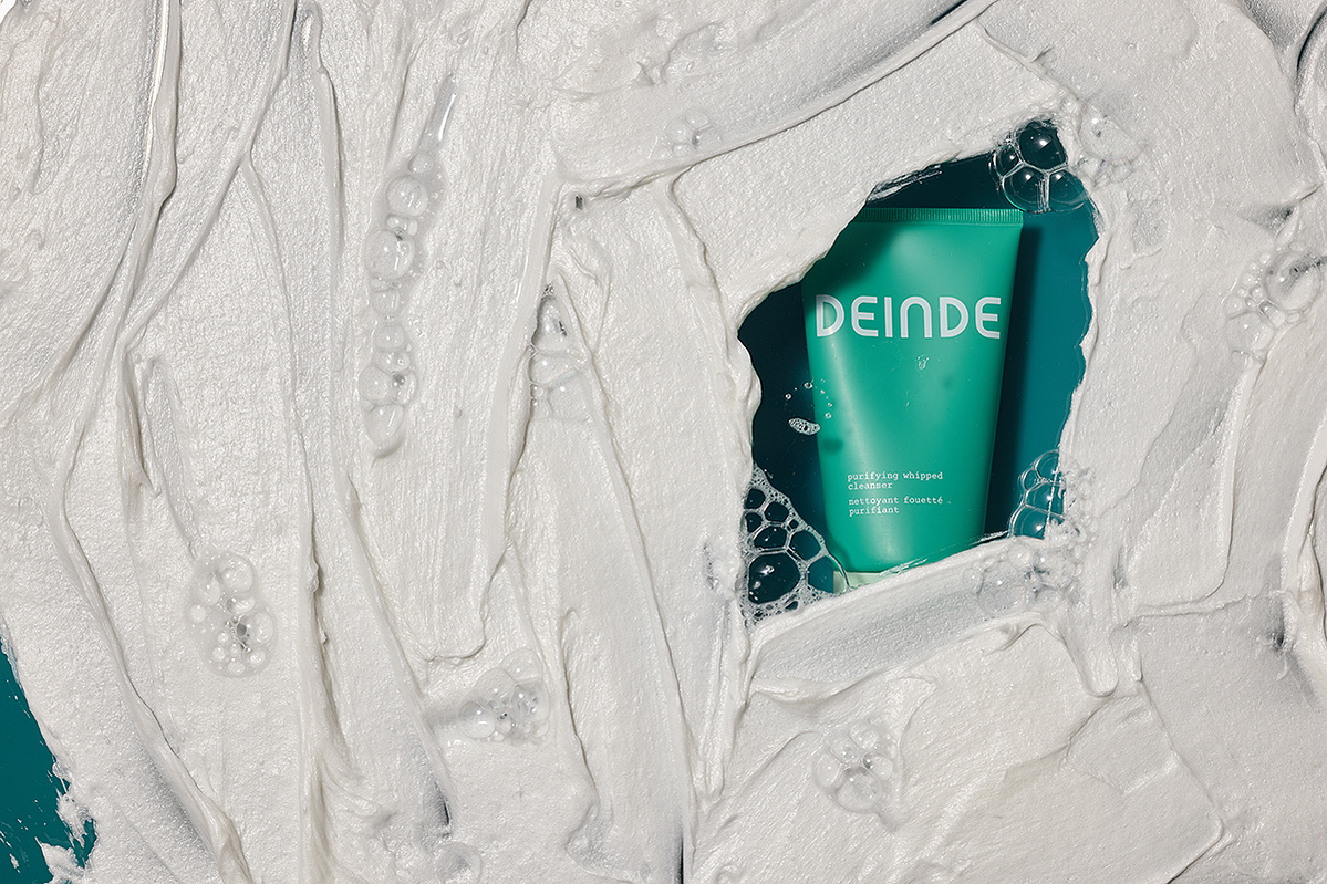 A conceptual product shot featuring Deinde skincare emerging from textured cream, symbolizing deep hydration and skin renewal. Photographed by Los Angeles product photographer Alex Kapustin at Rig Studio LA.