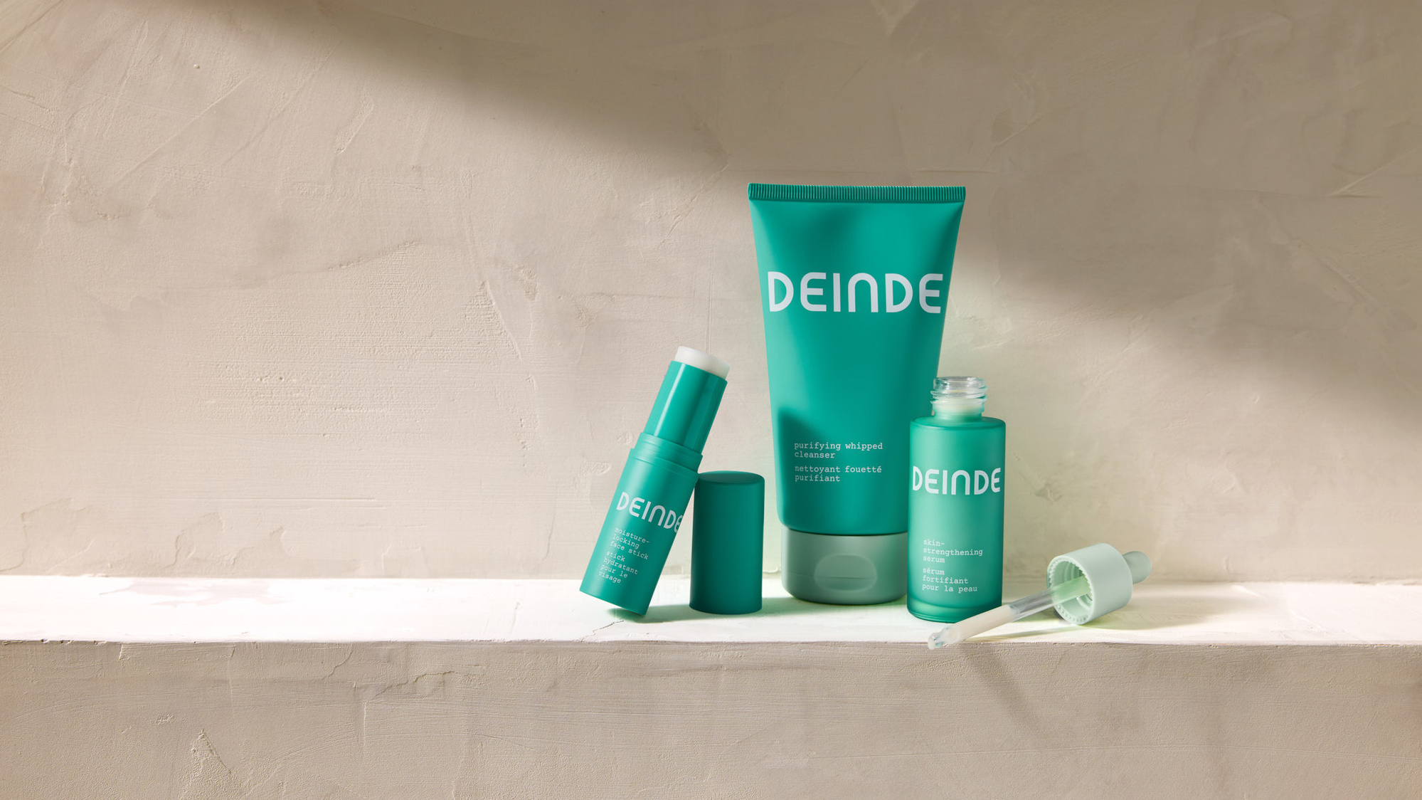 Deinde skincare products displayed on a textured stone ledge with soft natural lighting. The open serum bottle and dropper highlight the formula, while the clean aesthetic enhances the brand’s modern, minimalist appeal.