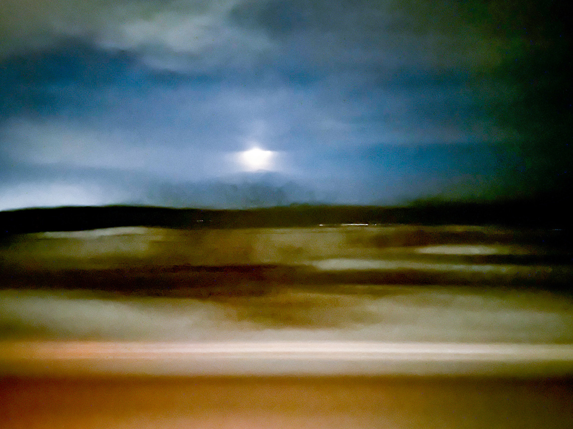 Blurred abstract landscape. Strips of colour from a field then dark band of trees in background. A blurry moon in the night sky