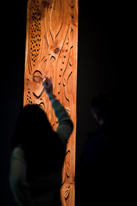 Un Visiteur d'exposition devant une grande sculpture de bois