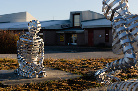 Une sculpture en aluminium représentant deux figure agenouillées l'une devant l'autre installée devant une école