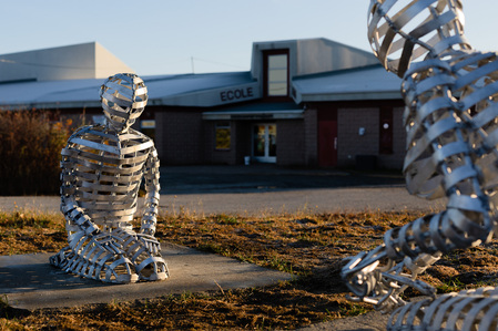 Une sculpture en aluminium représentant deux figure agenouillées l'une devant l'autre installée devant une école