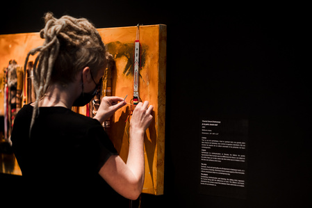 Une femme noue des noeuds sur une oeuvre collaborative dans une galerie d'art