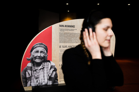Une jeune femme portant un casque d'écoute devant une installation d'exposition