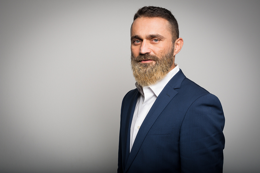 Modernes Businessportrait mit markanter Ausstrahlung. Der Mann trägt einen dunklen Anzug und blickt selbstbewusst in die Kamera. Der neutrale Hintergrund sorgt für einen professionellen Look – ideal für LinkedIn, Firmenprofile und Karriereportale.