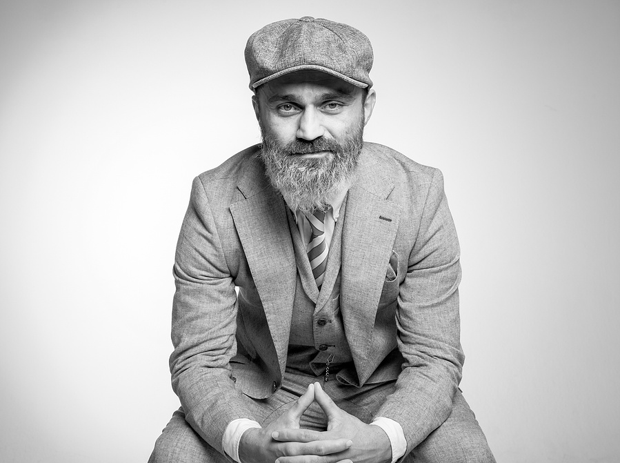 Charakterstarkes Schwarz-Weiß-Portrait im Retro-Look. Der Mann trägt einen eleganten Anzug mit Weste und Mütze, sein selbstbewusster Blick betont Persönlichkeit. Perfekt für künstlerische Portraitfotografie und Editorials.