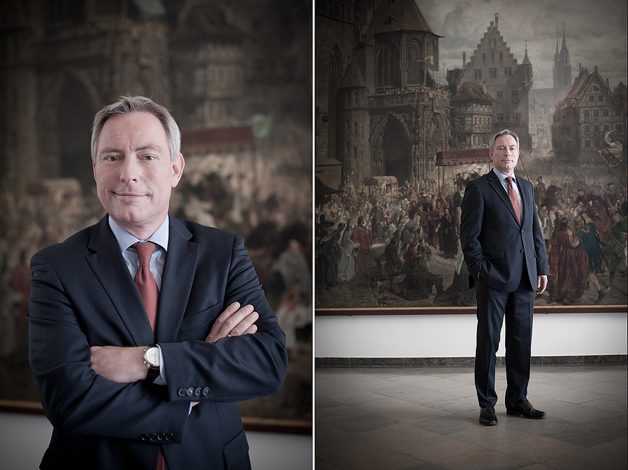 Stilvolles Businessportrait mit kunstvollem Hintergrund. Der Mann trägt einen eleganten Anzug und steht vor einem imposanten historischen Gemälde. Ideal für Führungskräfte, politische Profile oder exklusive Business-Shootings.