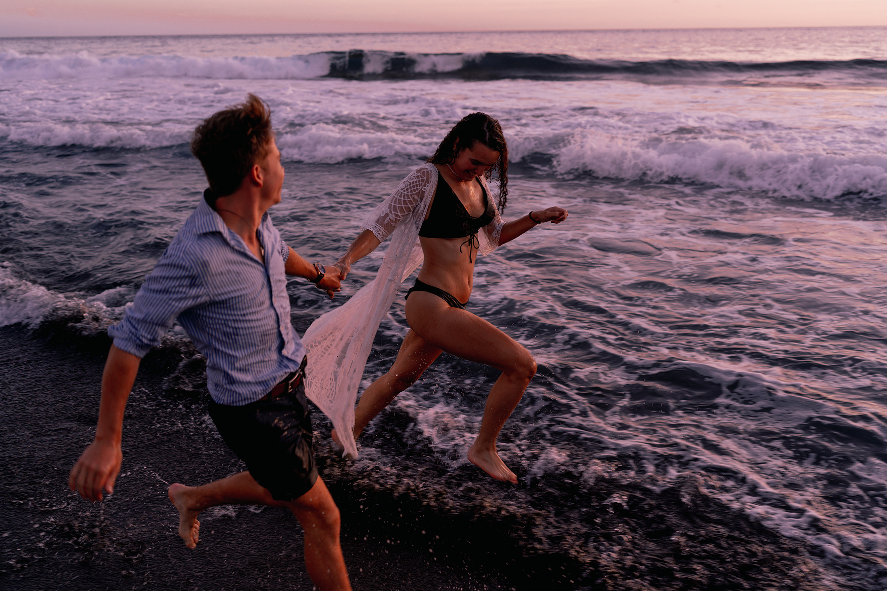 Deux amoureux courant sur une plage de sable noir à La Réunion pendant leur séance photos de couple.