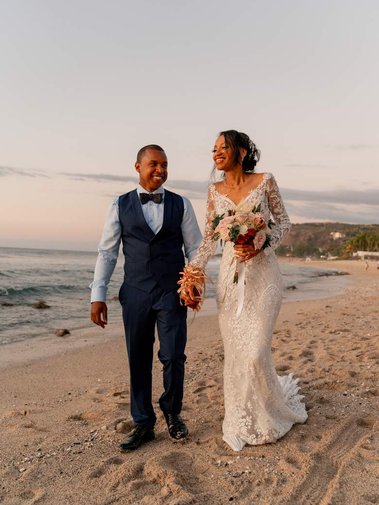 Des nouveaux mariés se promenant main dans la main sur une plage de sable blanc à La Réunion