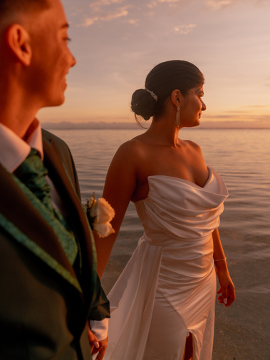 Des nouveaux mariés regardant l'horizon les pieds dans la mer. 