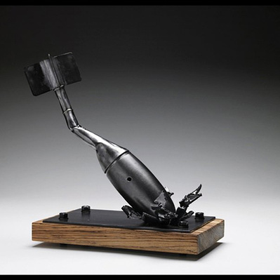 A steel and wood sculpture of a bomb as it hits the ground but does not explode