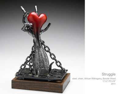 A steel and wood sculpture of a hand reaching out of an opening but restrained by 3 chains a carved wood heart rests on the hand