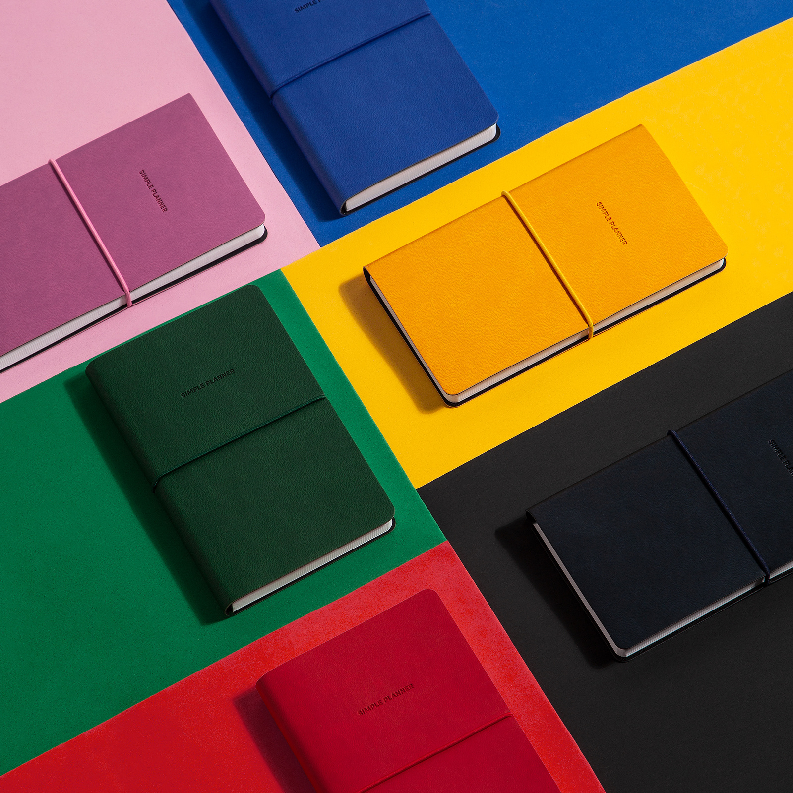 flatlay overhead stationery photography on a color blocked background of blue, pink, yellow, green, black and red, with corresponding colored notebooks on top styled in a geometric pattern.