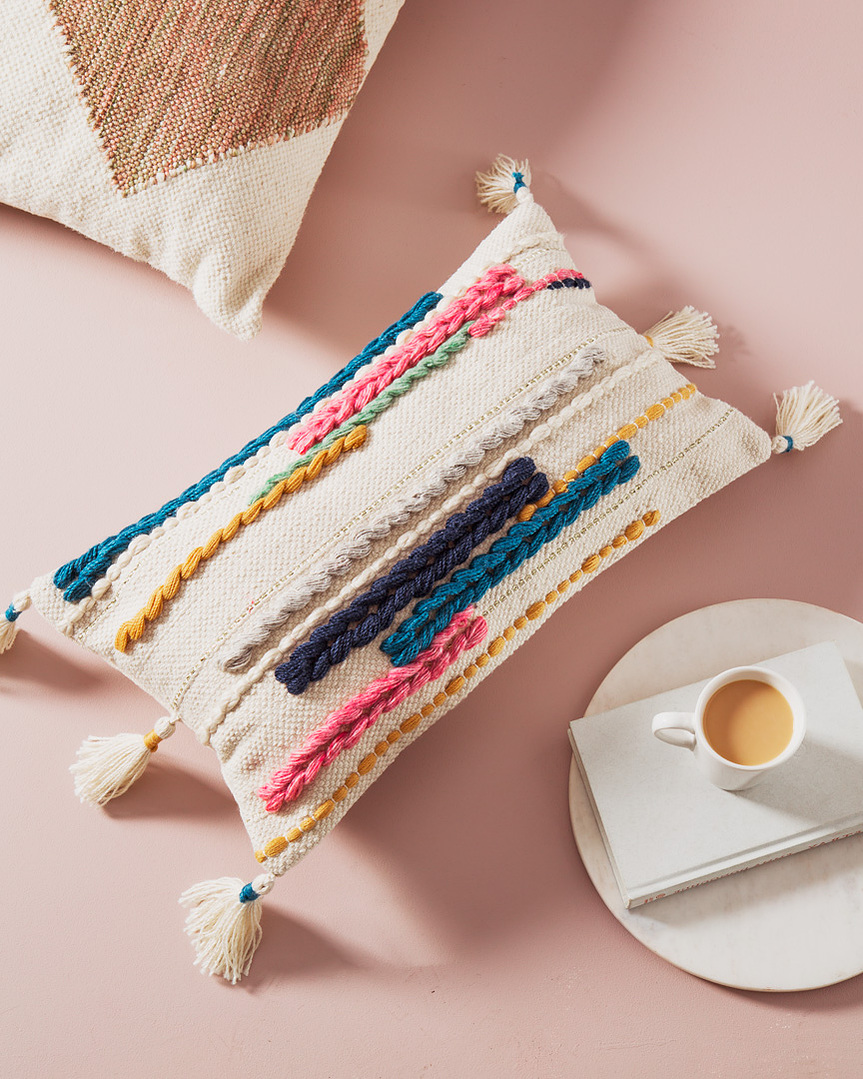 Environmental lifestyle photography of boho embroidered linen pillow product lifestyle on a pink background with marble dish, white book and white mug of coffee. 