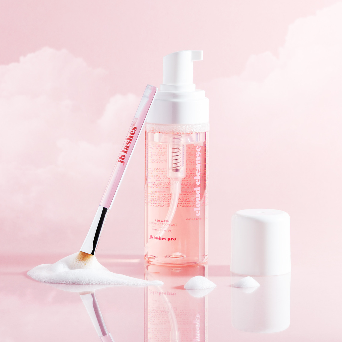 JB Lashes Pro Lash Wash Pump Bottle on Pink background with Clouds, cleansing brush sitting in foam suds with cap off product photography prop styling by photographer stylist Becca M los angeles