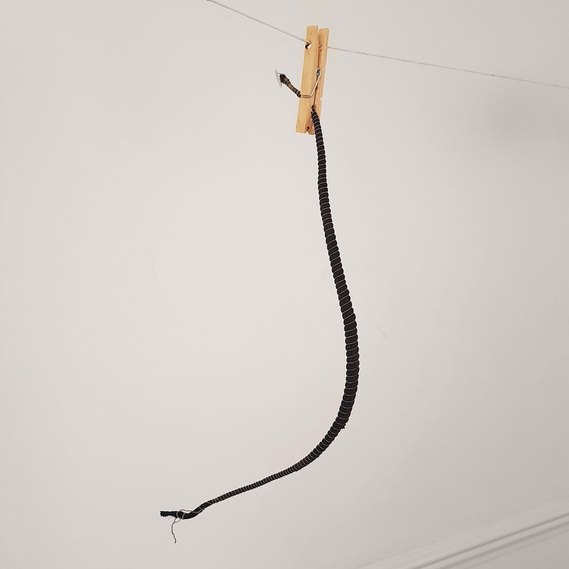 Black textile bracelet hanging from a wooden peg on a line.