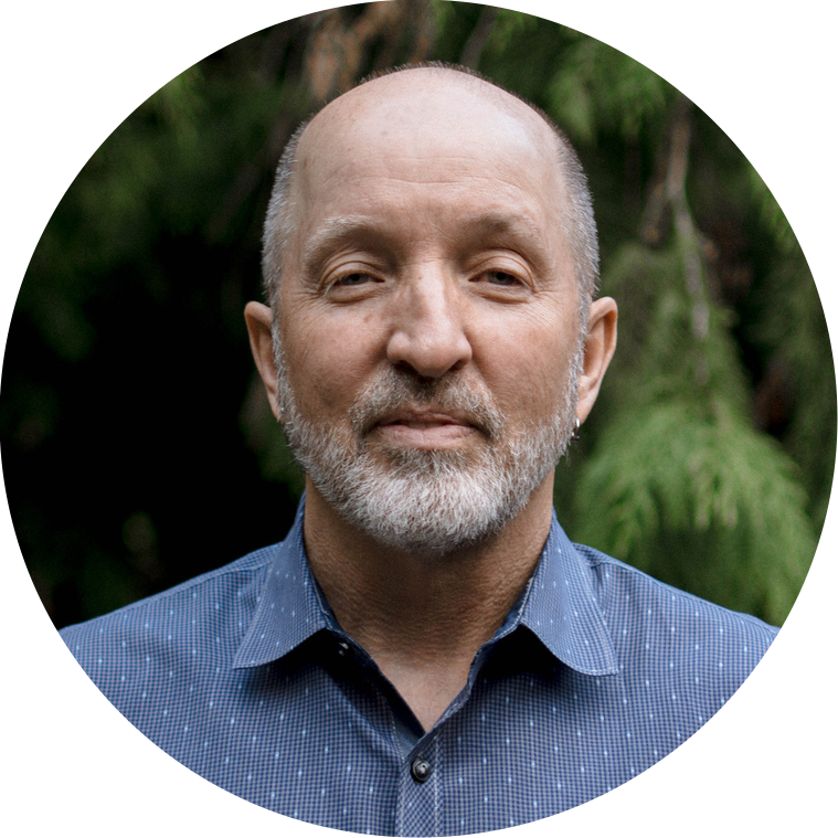 Integrative Guidance Coach and Author Doug Wheeler. A sixty-year-old man in a blue patterned button-up shirt against a forest backdrop. 