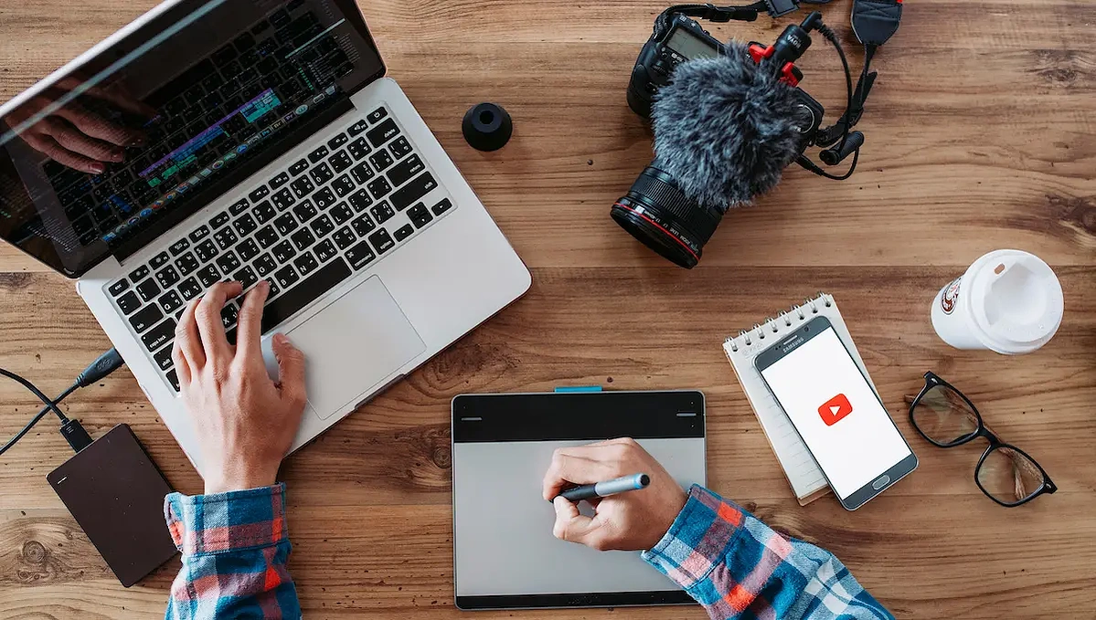 Individual working on content marketing strategies with a computer, camera, and phone.