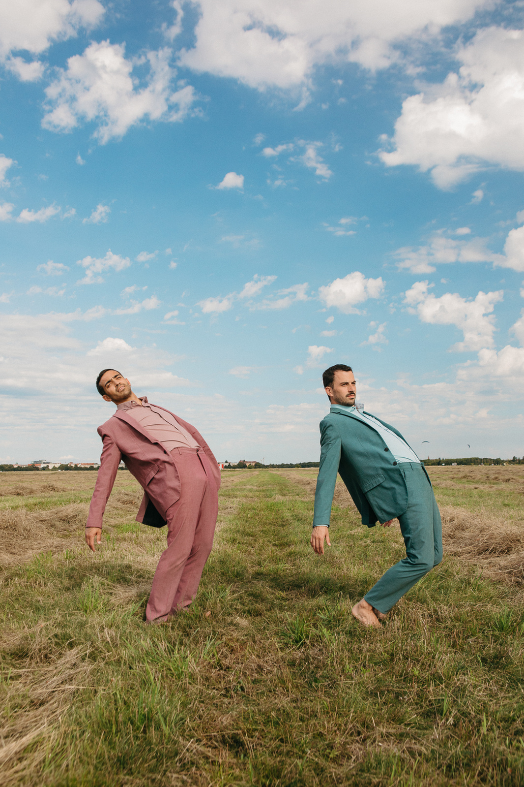 Two men dance in pastel-colored clothing in an open field