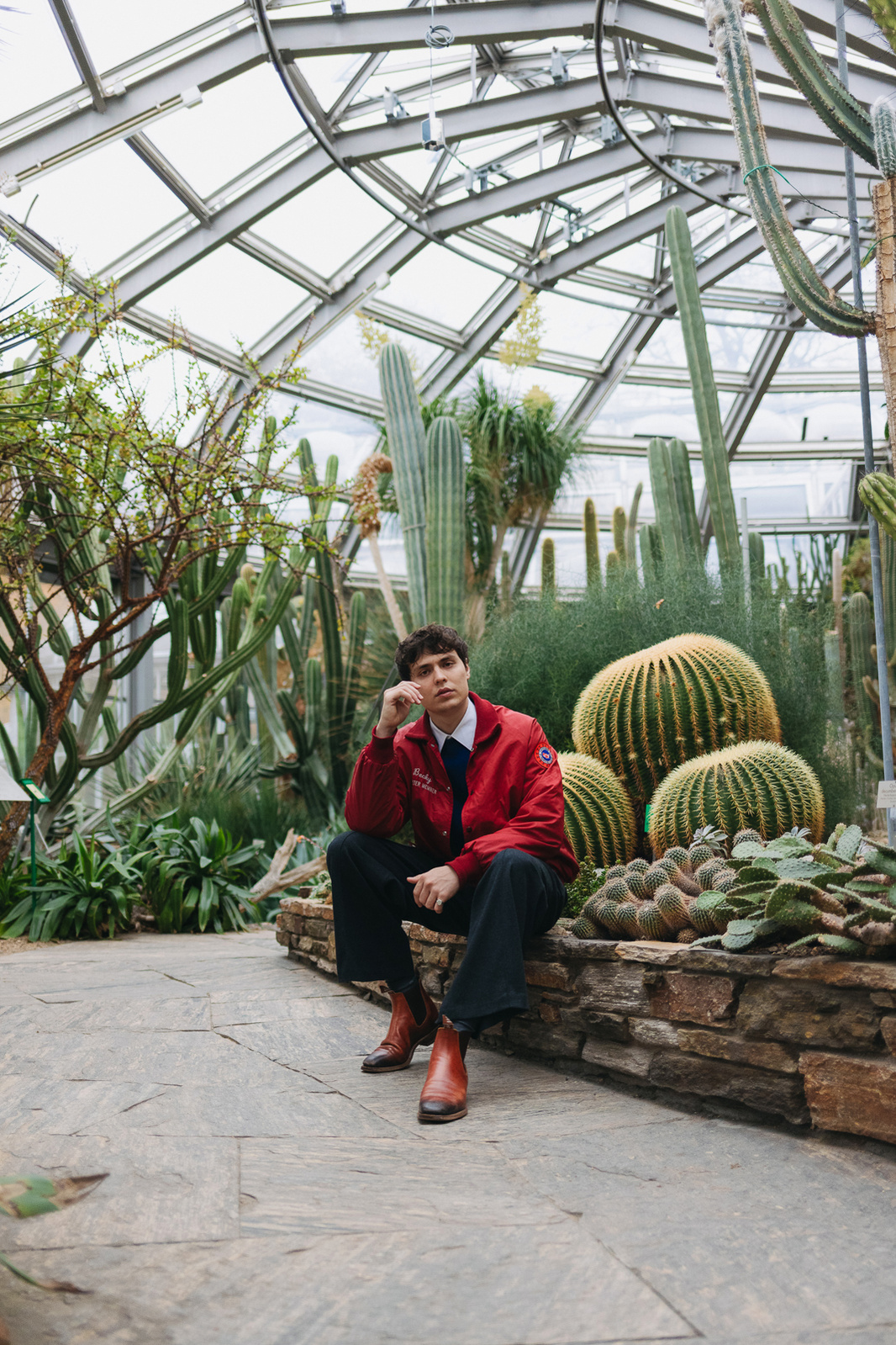 Man in red jacket sitting on a rock with cactus in background