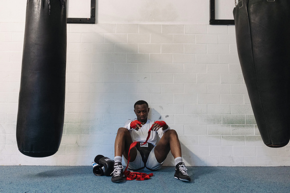 afro man sitting on the floor surrounded by punching bags removing the red bandages from his hands