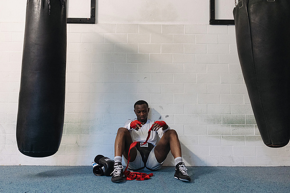 afro man sitting on the floor surrounded by punching bags removing the red bandages from his hands