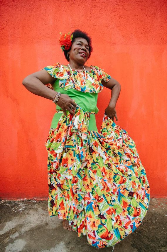 Afro woman dancing in her flower dress in front of an orange wall