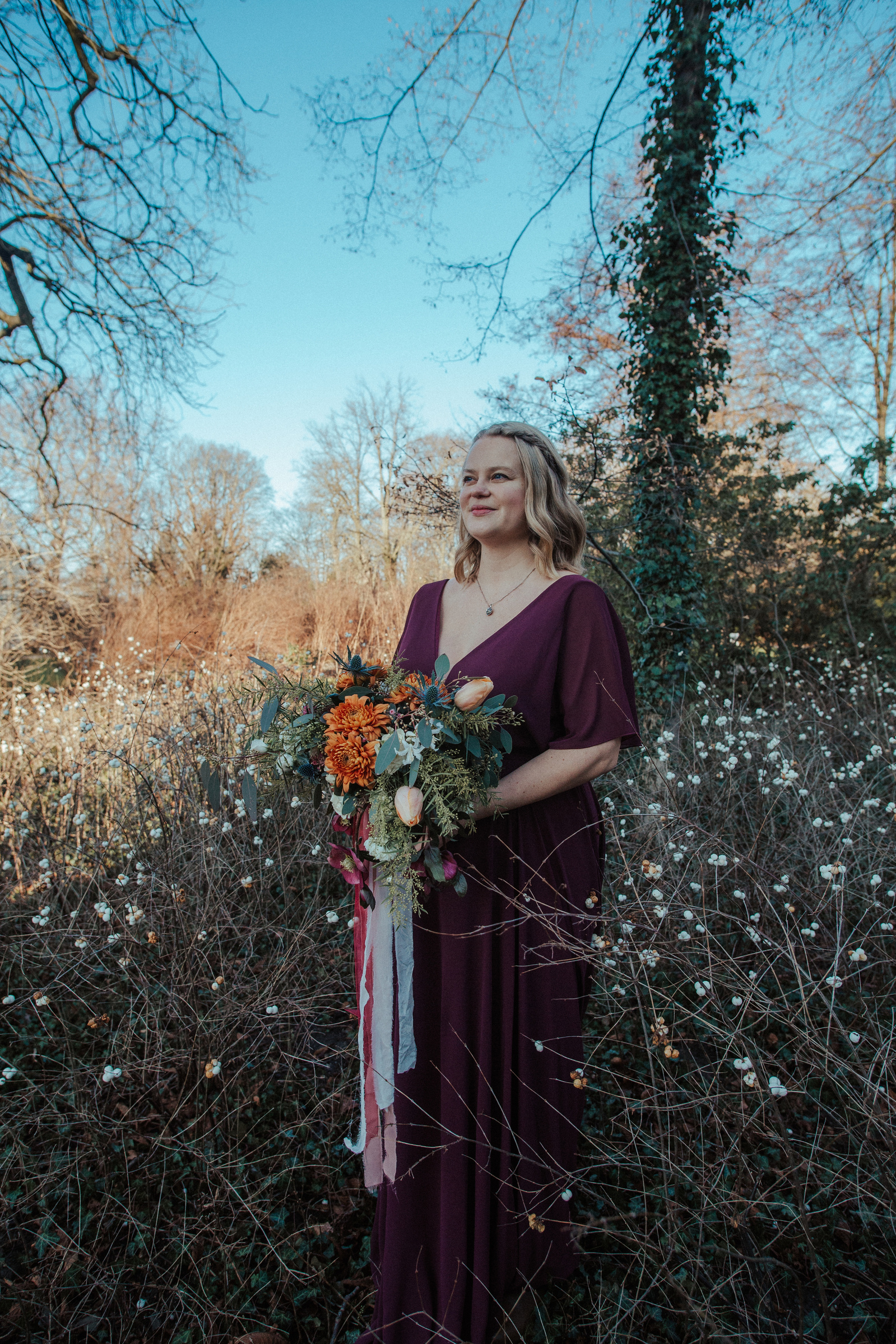 woman in red dress looking at the horizon in a field of roses holding a bouquet of flowers
