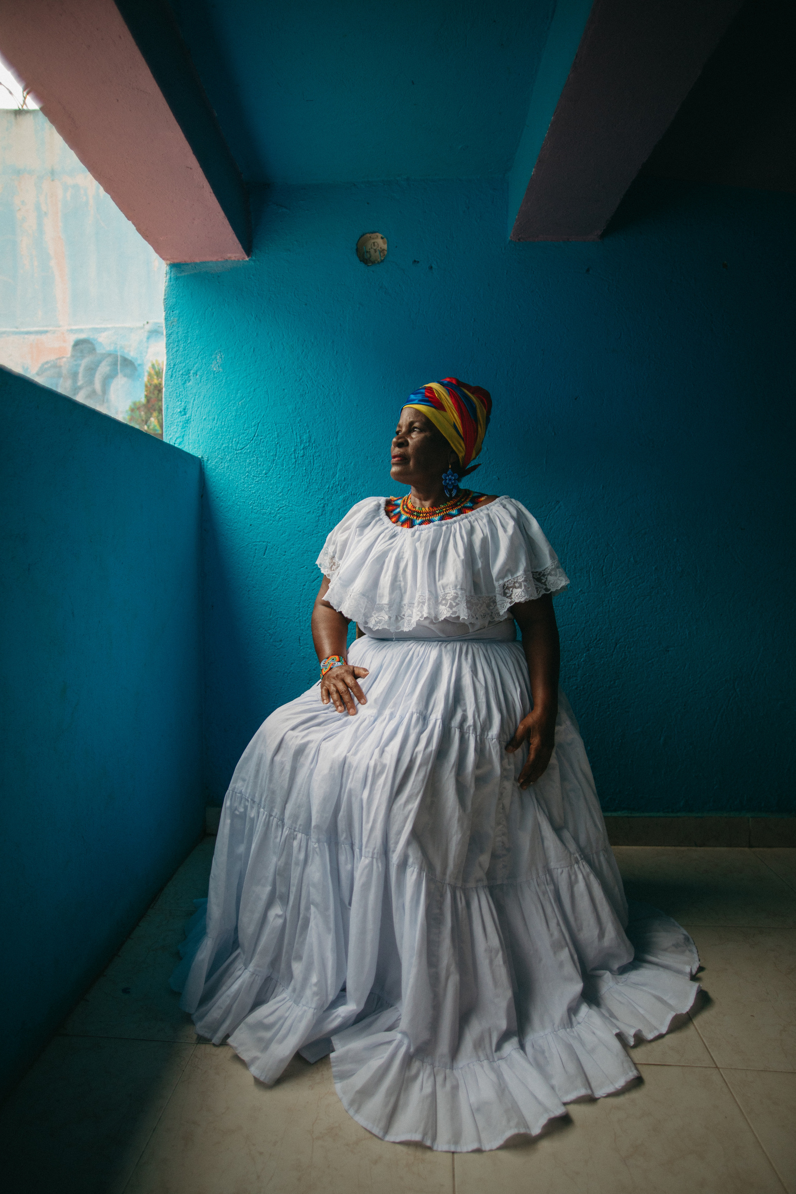 African-American woman in white dress sitting in front of a blue background.