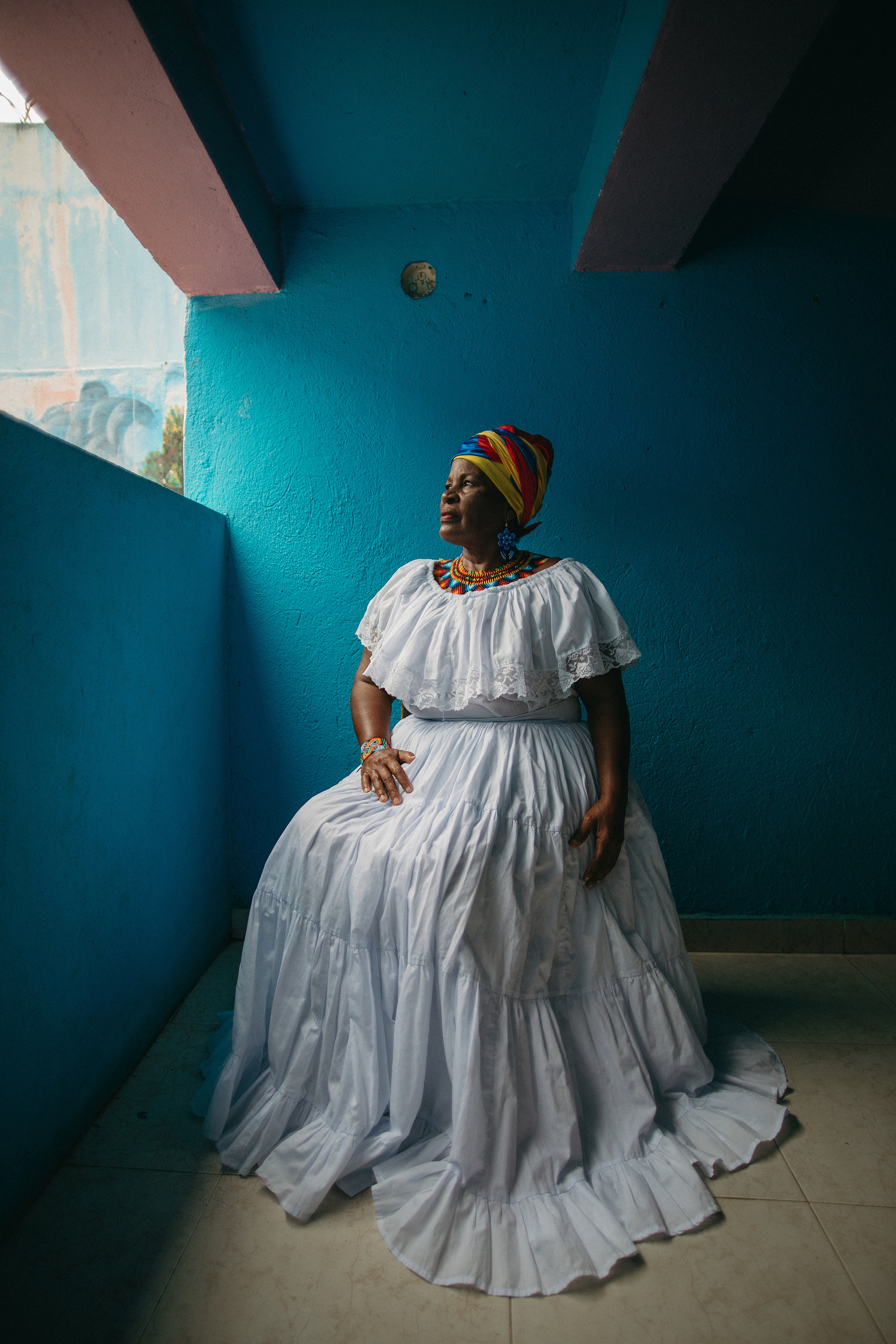 African-American woman in white dress sitting in front of a blue background.
