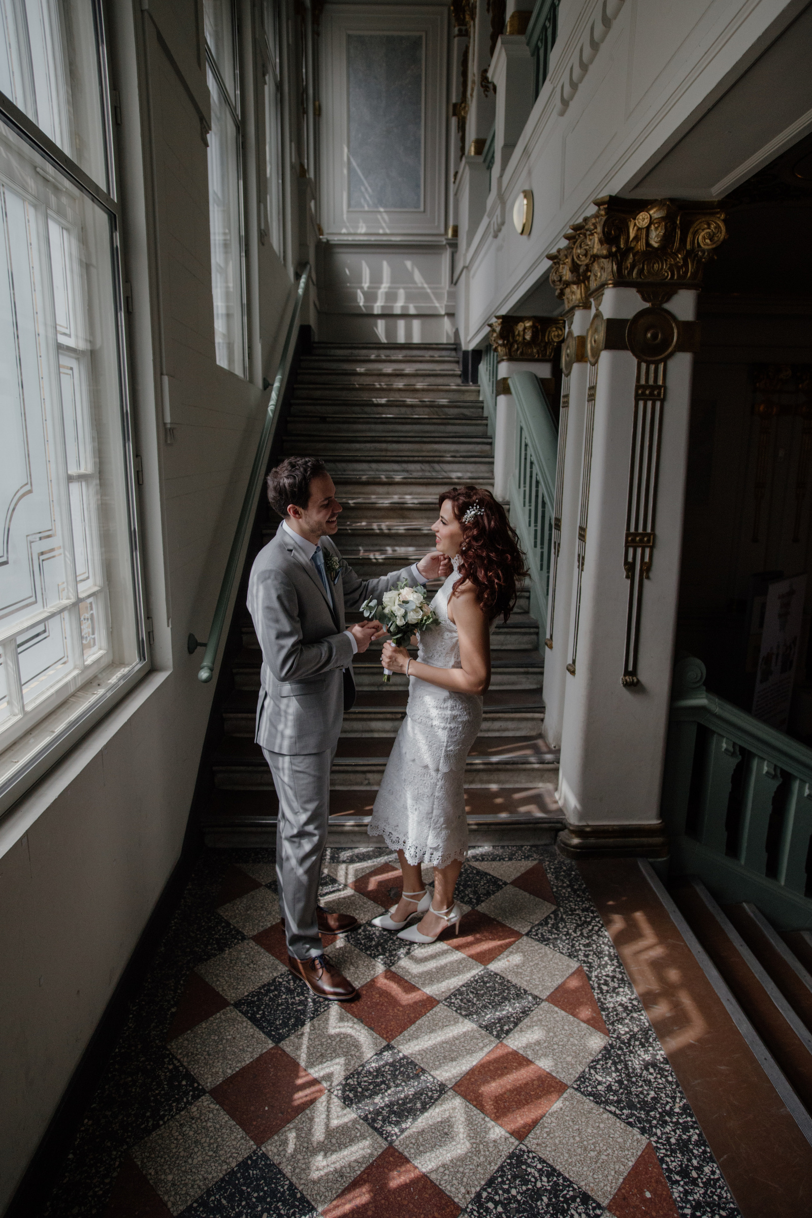 newly married couple look at each other in front of a large window with lots of light.